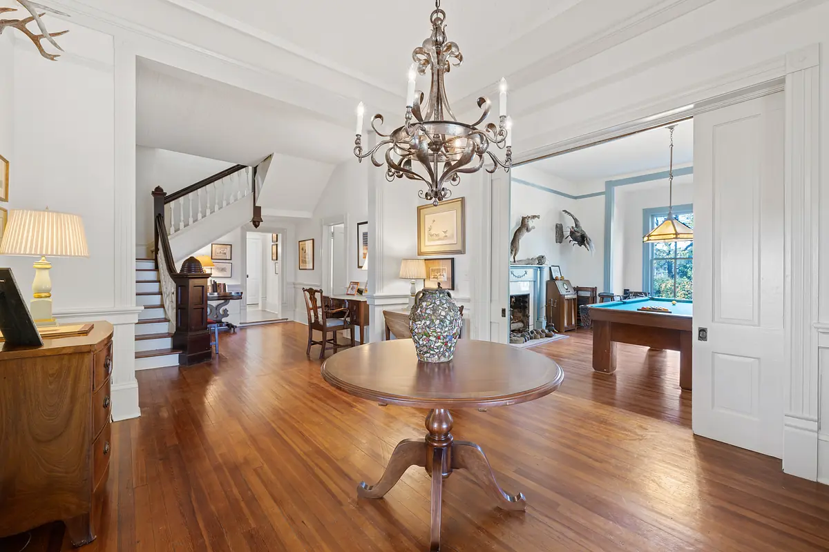 Foyer with round wooden table, decorative vase, staircase, chair, and large window for natural light