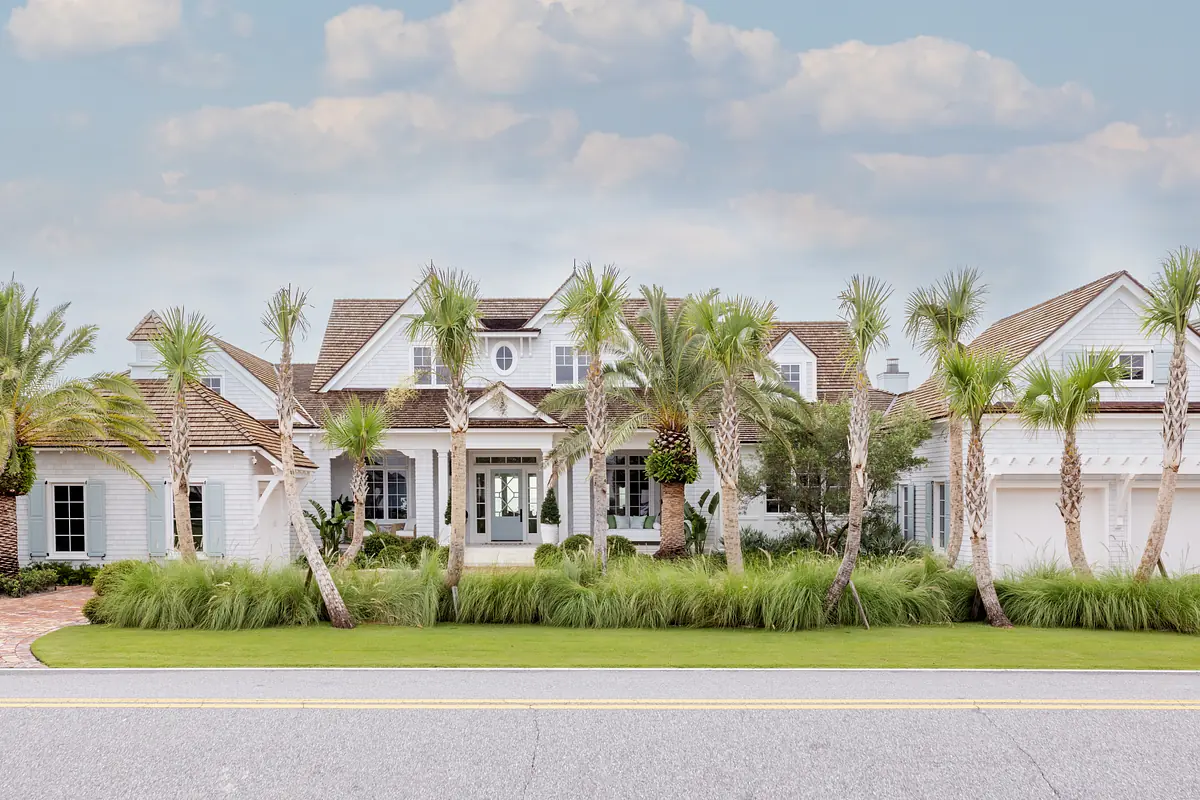 Front exterior of a house with palm trees, landscaped yard, double doors, and pitched roofs.