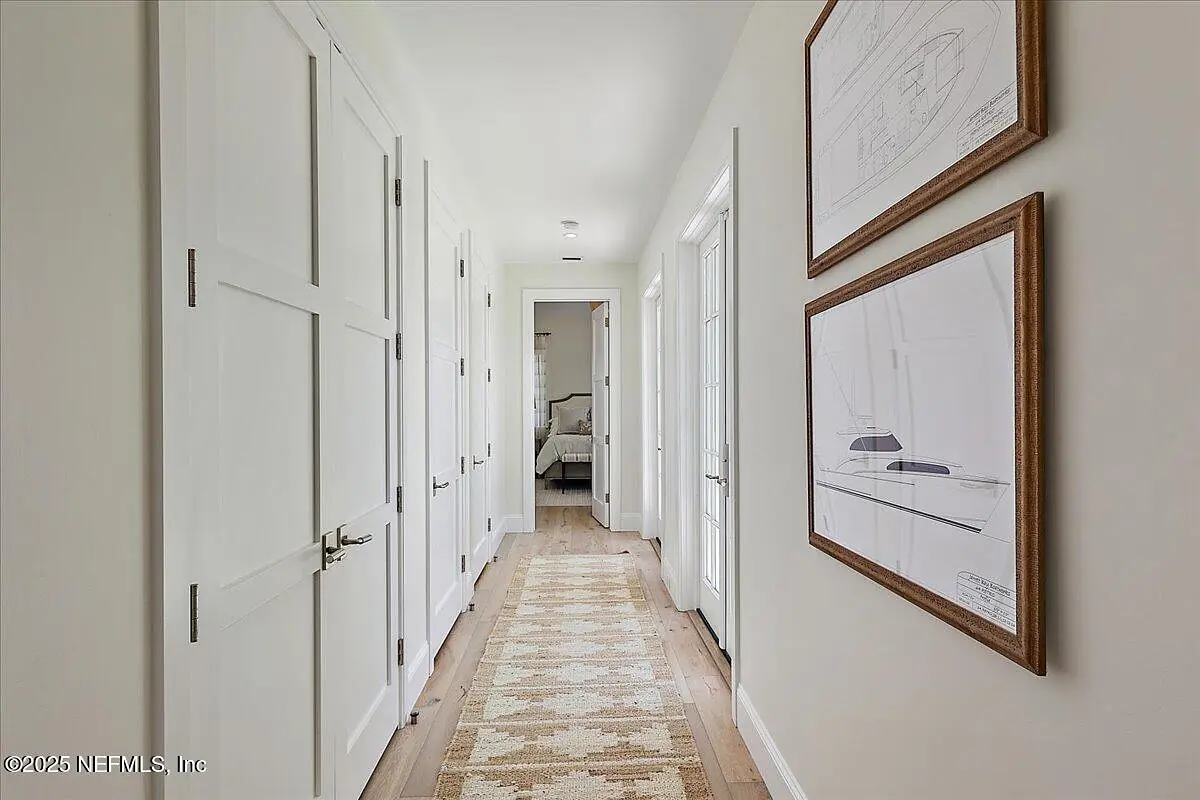 Hallway with white walls, doors, patterned rug, and framed sketches.