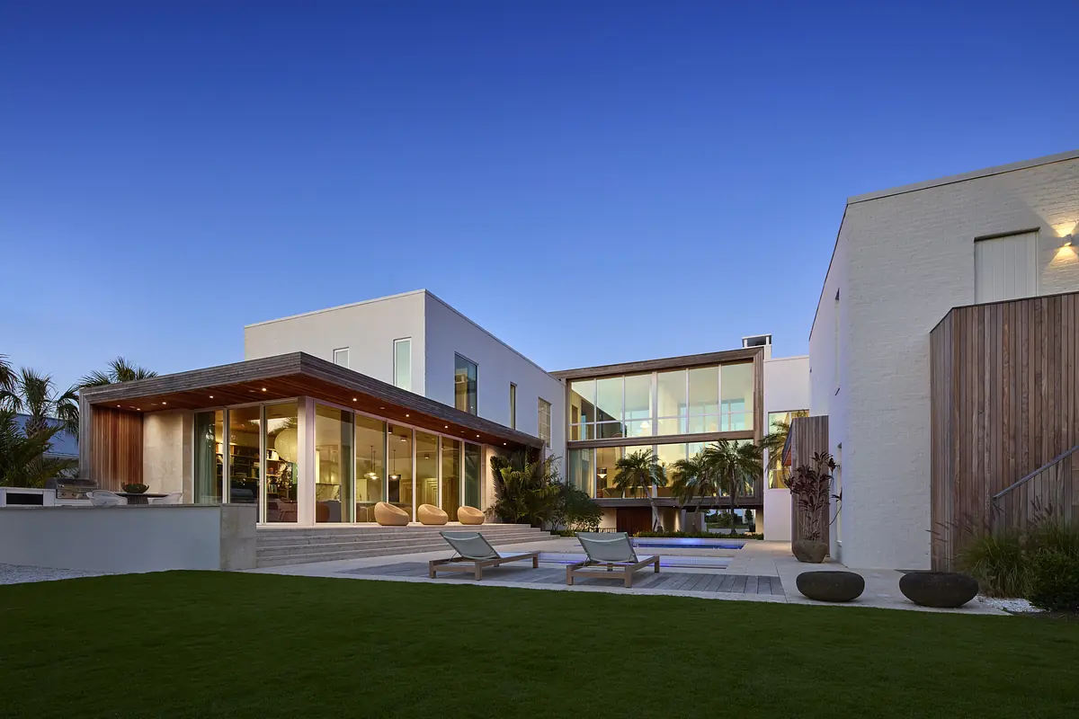 Exterior rear with large windows, patio, lounge chairs, and swimming pool surrounded by tropical plants.