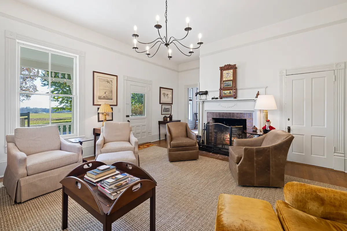 Living room with armchairs, brown sofa, coffee table, fireplace, large windows, and artwork.