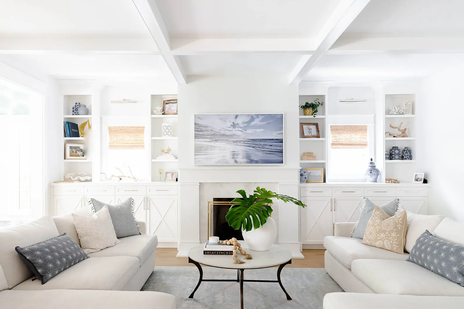 Living room with white sofas, round coffee table, built-in shelves, television, and green plant.