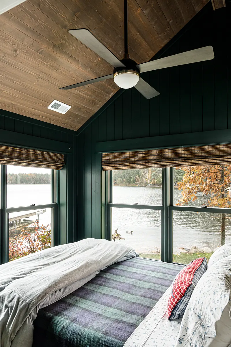 Bedroom with bed, plaid throw, large windows, wooden trim, and vaulted ceiling with ceiling fan.