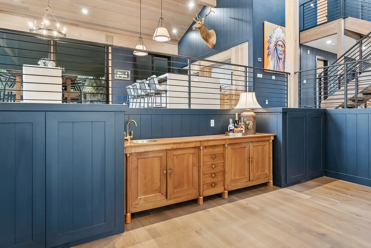 Space with wooden sideboard, dark blue paneled wall, lamp, and stair railing in a light wood environment