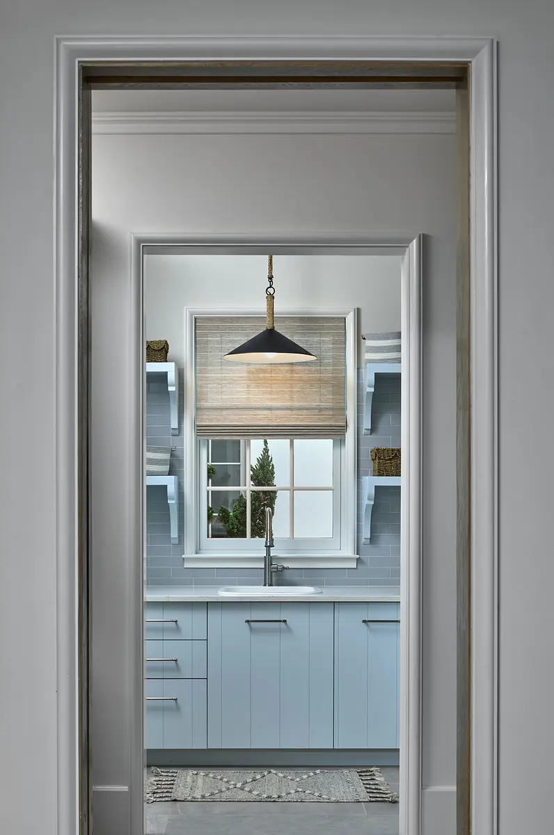 Kitchen with light blue cabinetry, stainless steel sink, window, and pendant light.