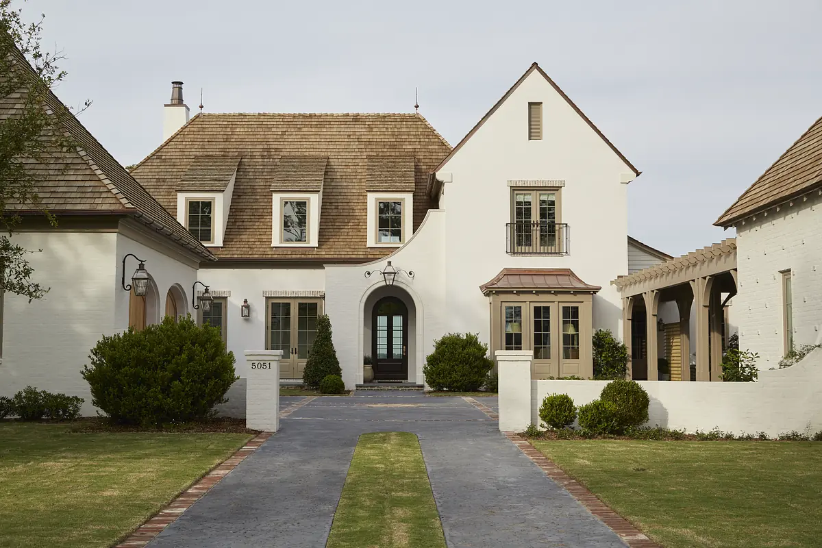 Front exterior view of a house with stone, stucco, pitched roof, double door entrance, and landscaped yard.