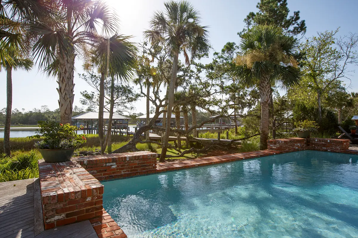 Exterior yard with swimming pool, brick edge, palm trees, and wooden dock in the background