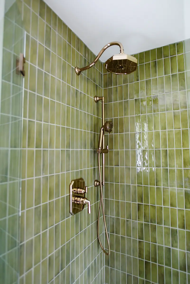 Bathroom shower with green tiles, rainfall showerhead, handheld shower, and brass control panel.