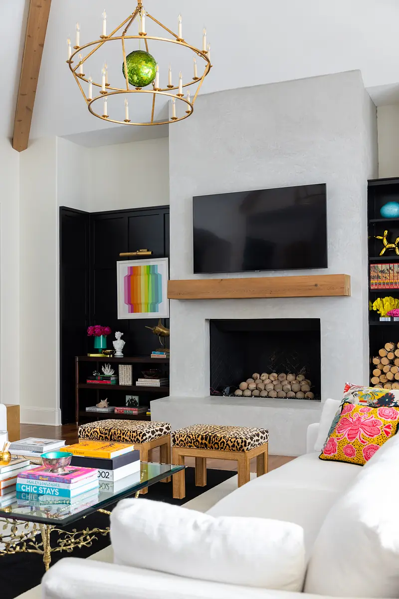 Living room with white sofa, glass coffee table, animal print stools, black shelving unit, and stone fireplace with natural light
