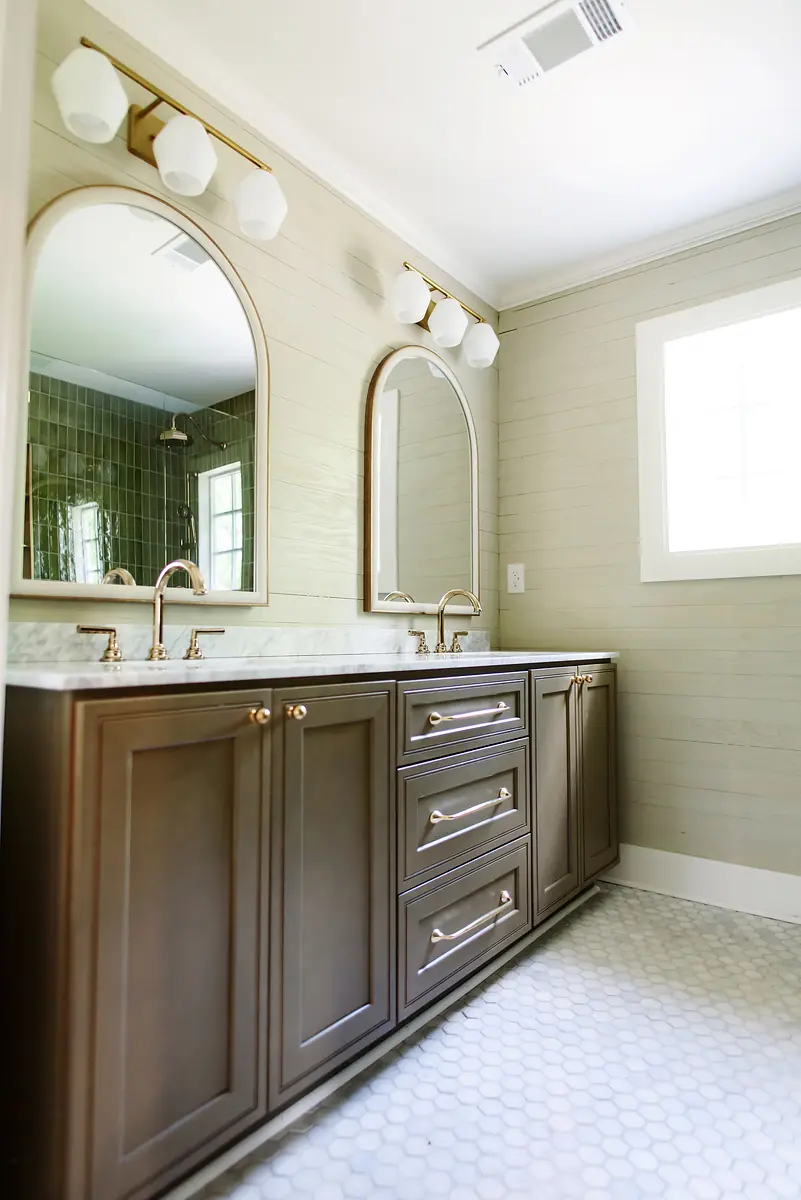 Bathroom with double vanities, marble countertop, round mirrors, and hexagonal tiled floor.