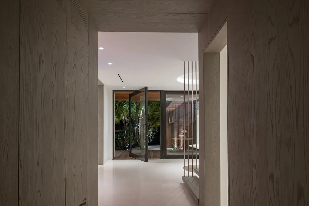 Hallway with light wood walls, white floor, glass doors, and vertical slat partition