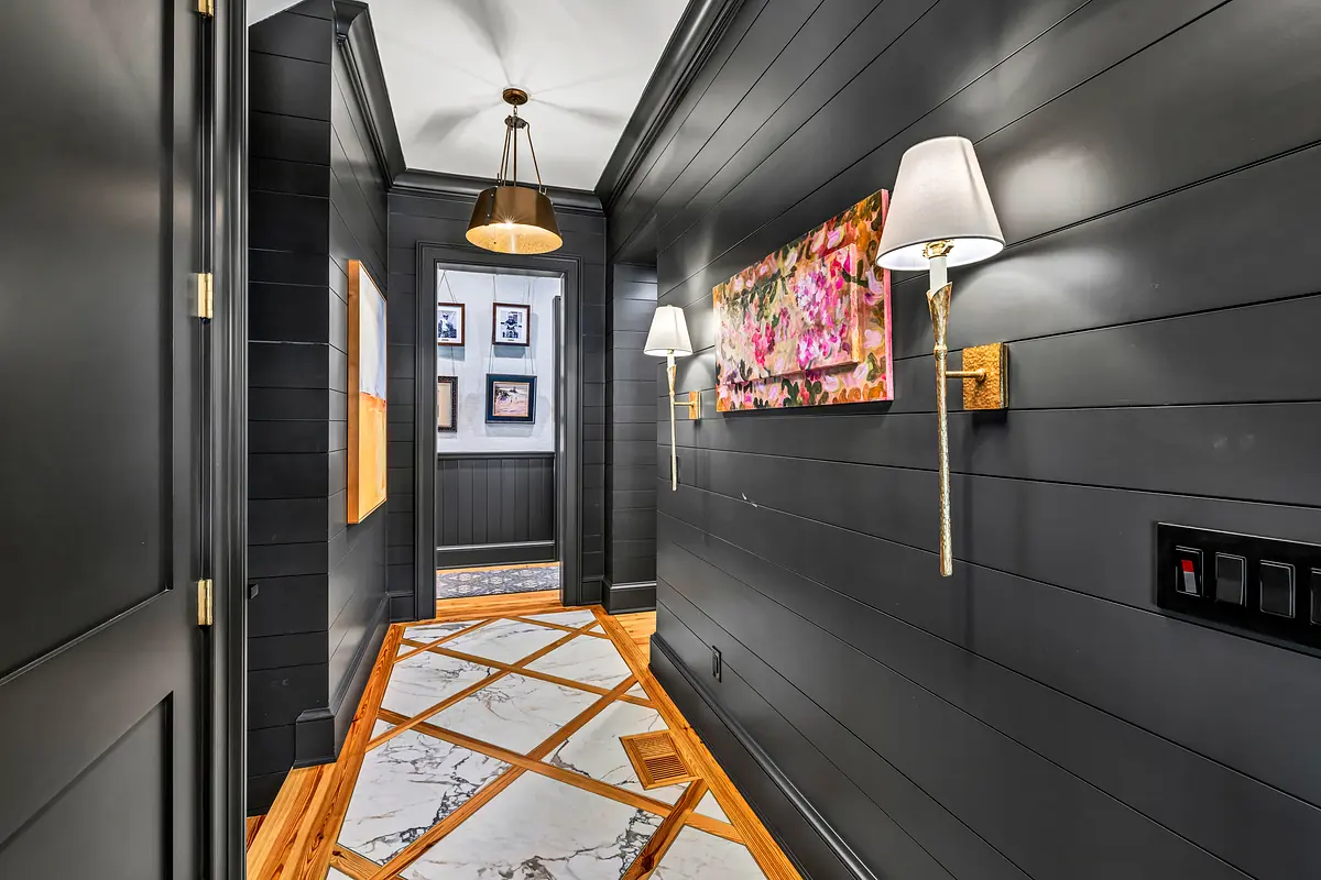 Hallway with dark paneling, marble flooring, wall sconces, and a pendant light.