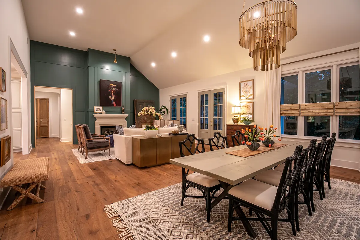 Dining room with long table, upholstered chairs, area rug, and seating area with a sofa and fireplace.