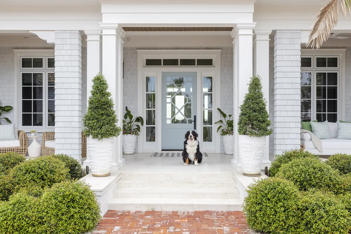 Exterior front with white columns, light blue door, topiary shrubs, and a dog on the steps.