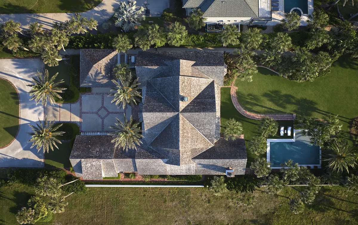 Aerial view of a home with gabled roof, palm trees, lawn, driveway, and swimming pool.