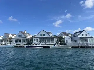 Row of waterfront houses with gable roofs, large windows, porches, and boats at docks.