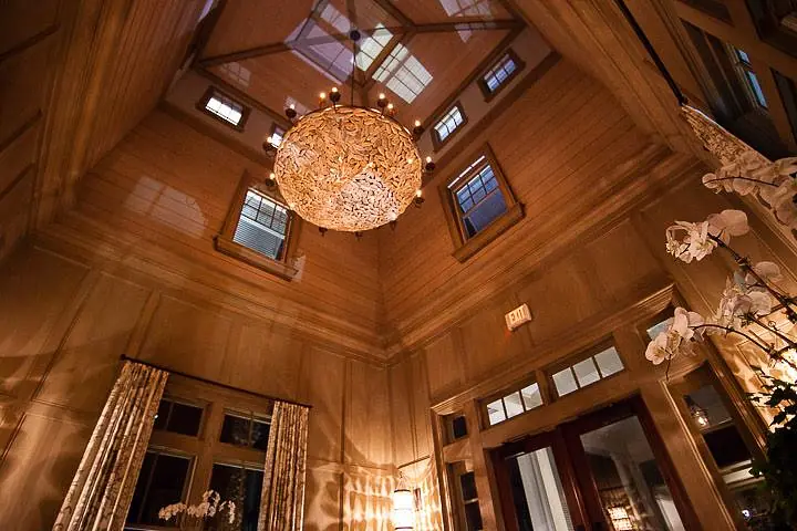 Foyer with chandelier, high ceilings, wall paneling, large windows, double doors, and white orchids.