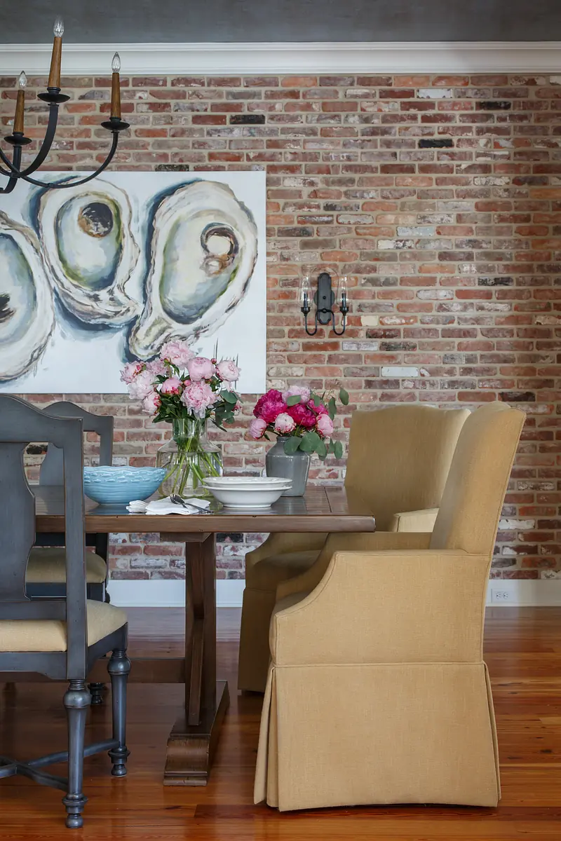 Dining room with wooden table, armchairs, side chairs, wall art, and floral arrangements.