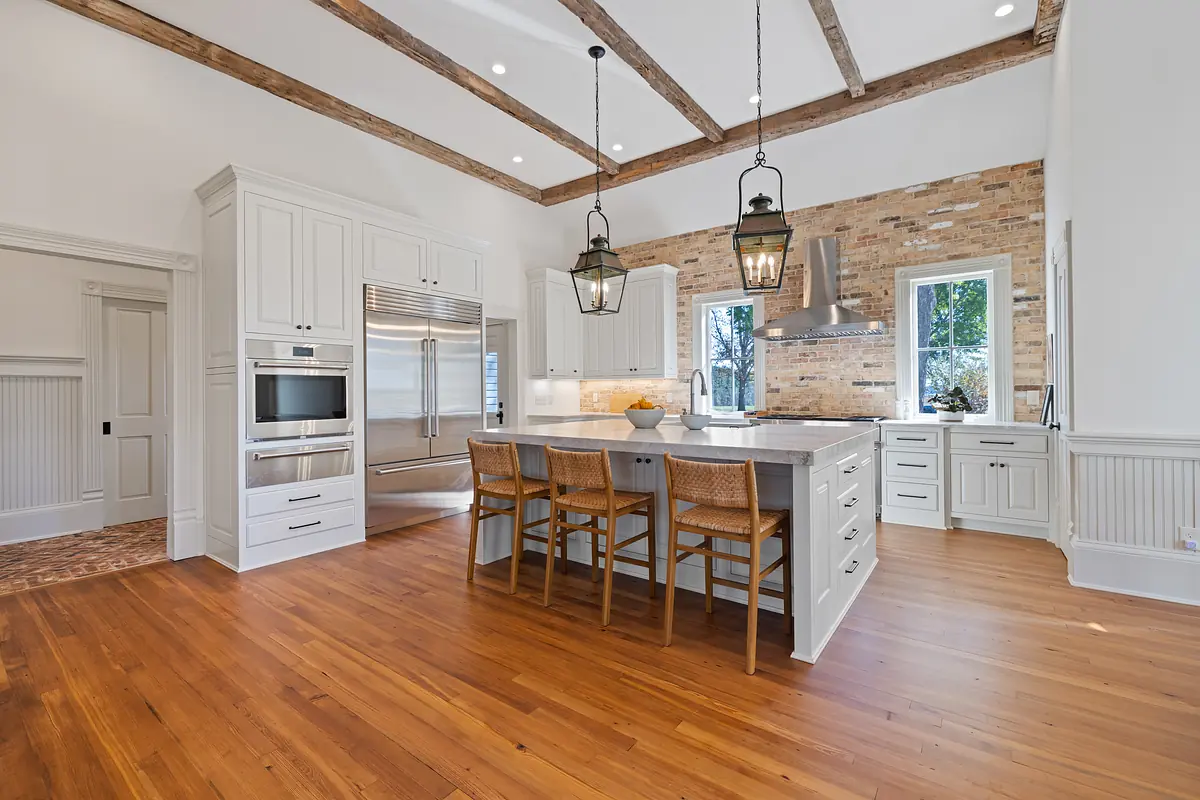 Kitchen with island, stools, white cabinetry, brick wall, and wooden beams