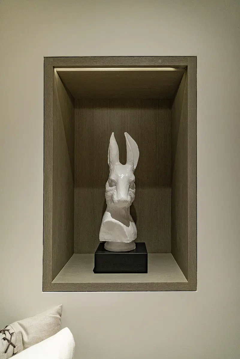 Wall niche with white rabbit head sculpture on a black base, illuminated by light above.
