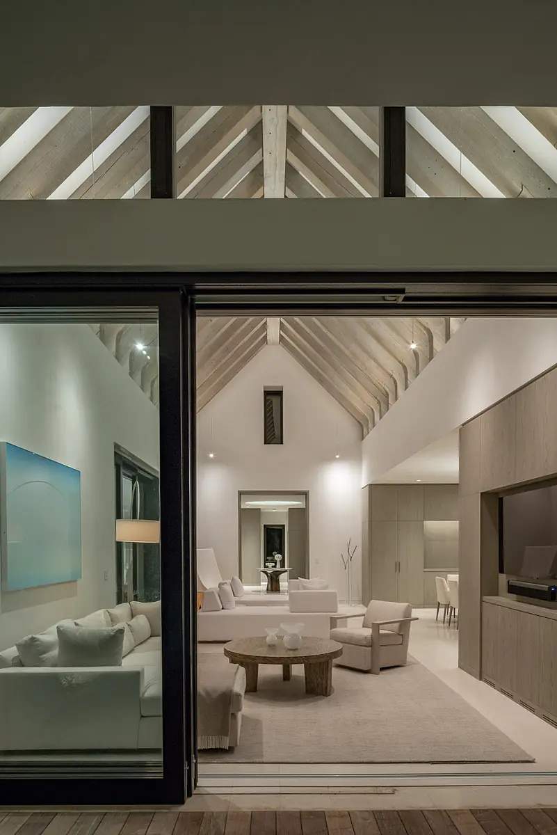 Living room with light sofa, armchair, coffee table, large windows, and vaulted ceiling with beams.