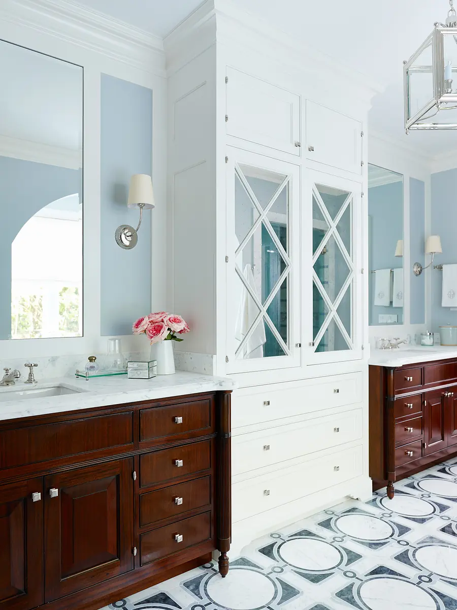 Bathroom with double vanity, marble countertop, mirrors, wall sconces, and patterned tile flooring.