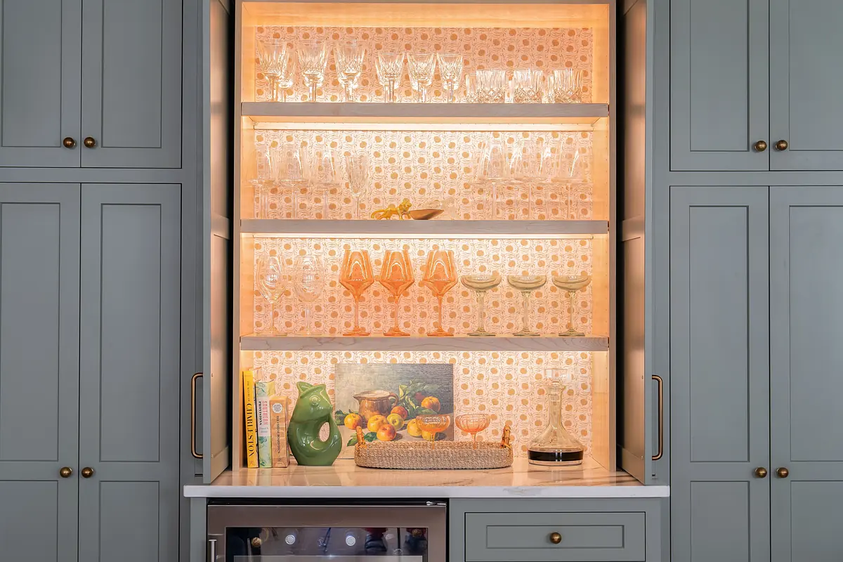 Kitchen with glassware on shelves, gray cabinetry, and countertop items including a green pitcher and decorative basket.
