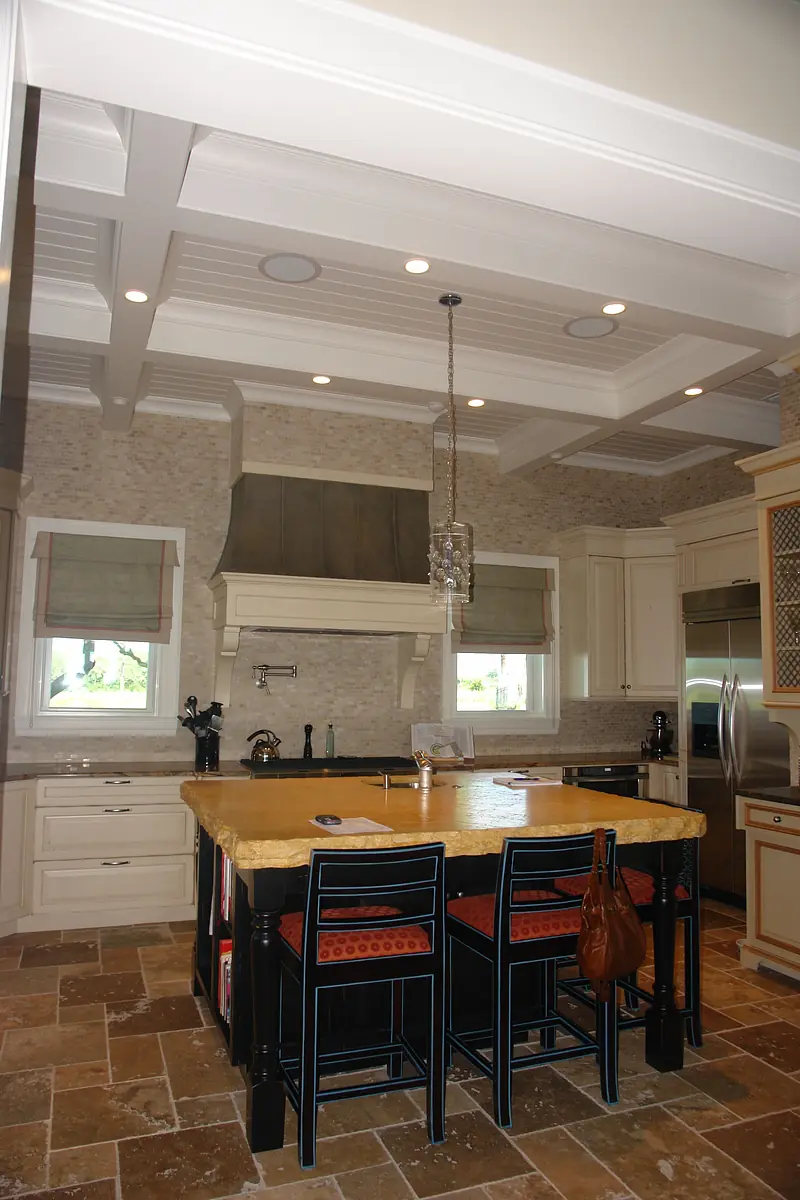 Kitchen with large island, bar stools, cabinetry, stone walls, and stainless steel appliances.