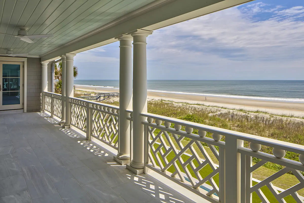 Exterior deck with white columns, lattice railing, light tiles, and view of the beach and ocean.