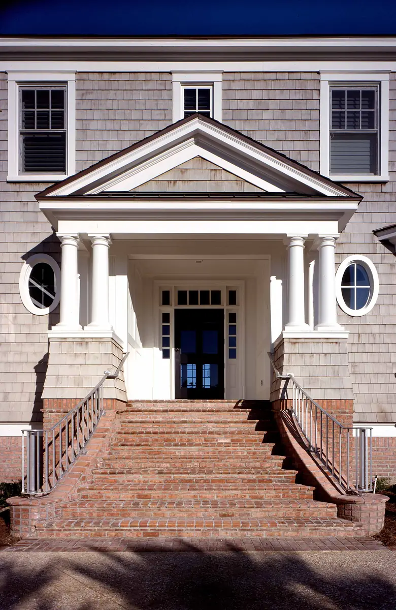 Exterior front entry with brick steps, double-door entrance, white columns, and circular windows.