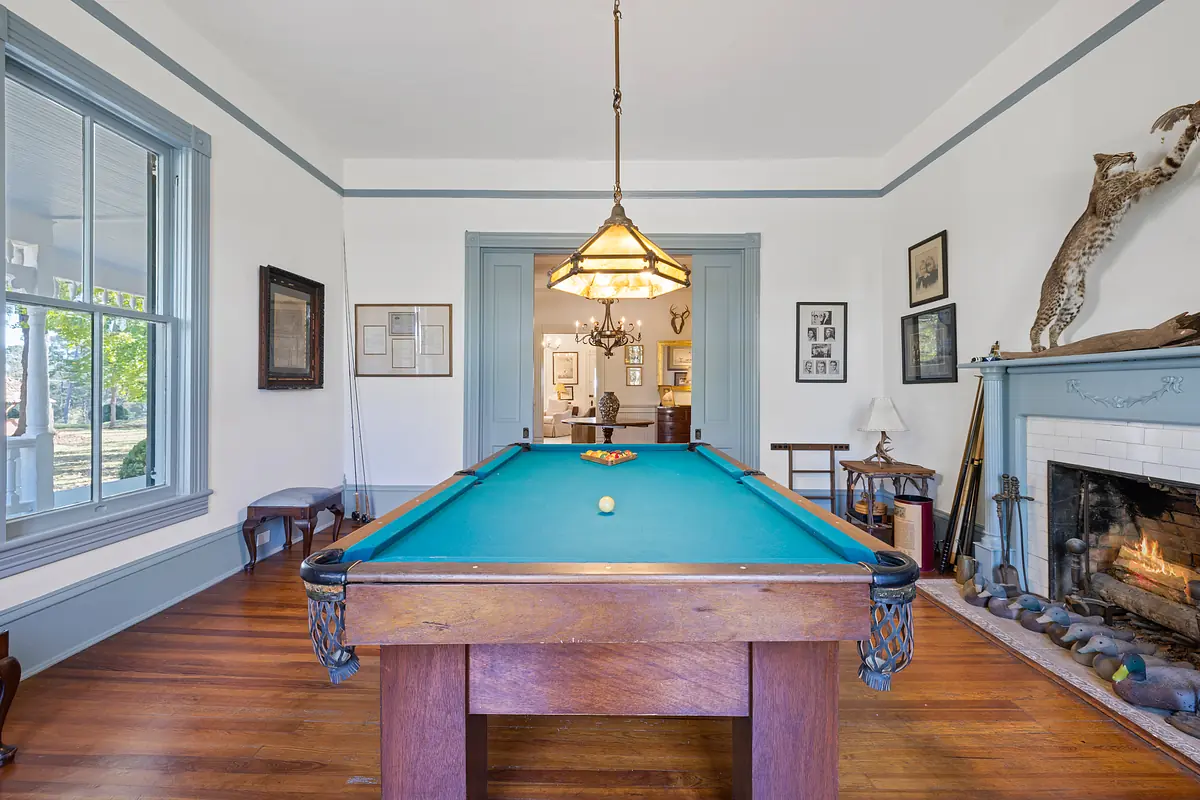 Room with billiard table, fireplace, artwork, and natural light from large windows.