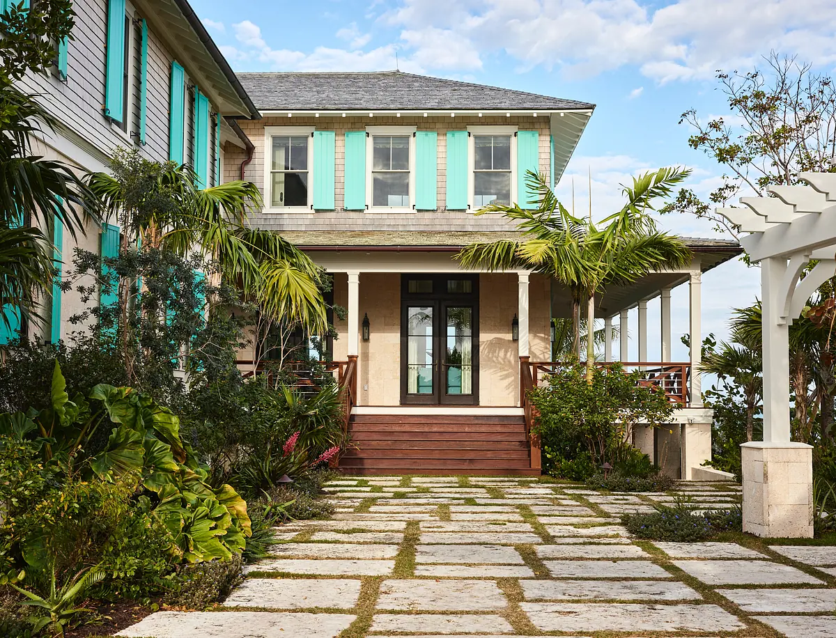 Exterior front entrance with wooden steps, double door, turquoise shutters, stone pathway, and surrounding greenery.