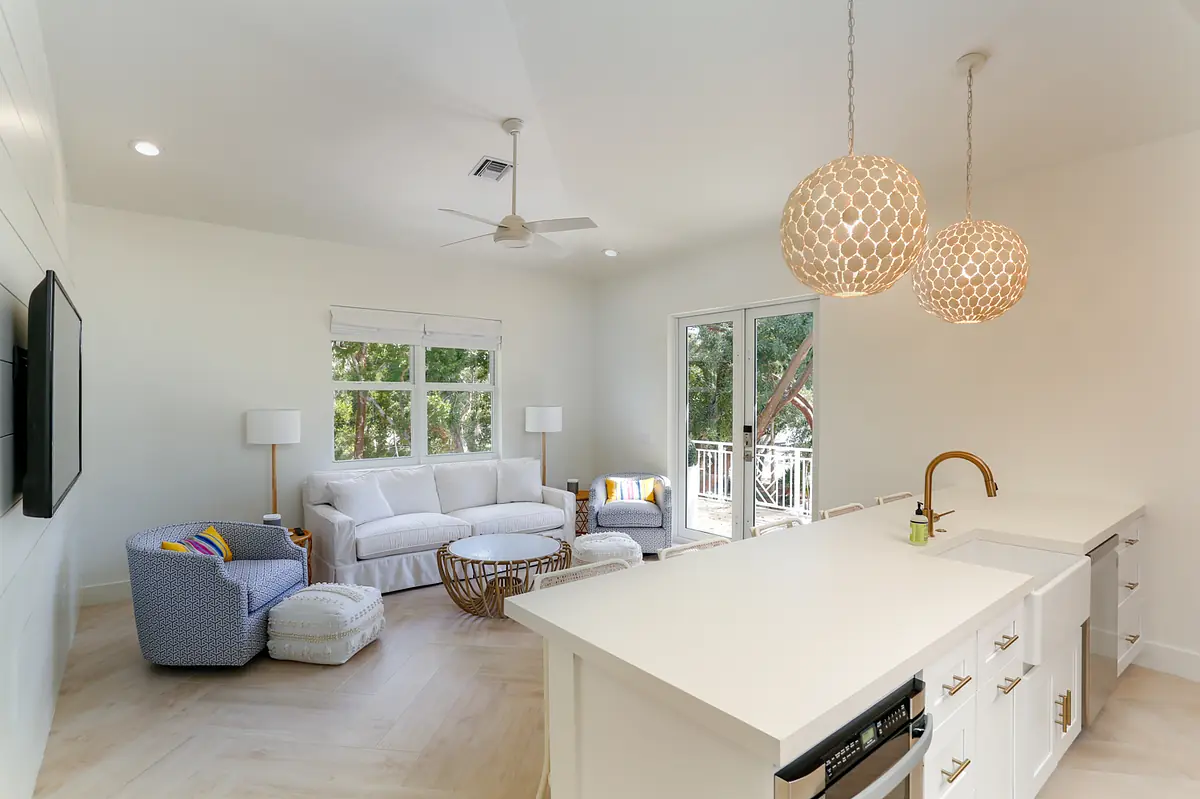 Living room with white sofa, blue armchair, wicker coffee table, large windows, and ceiling fan.