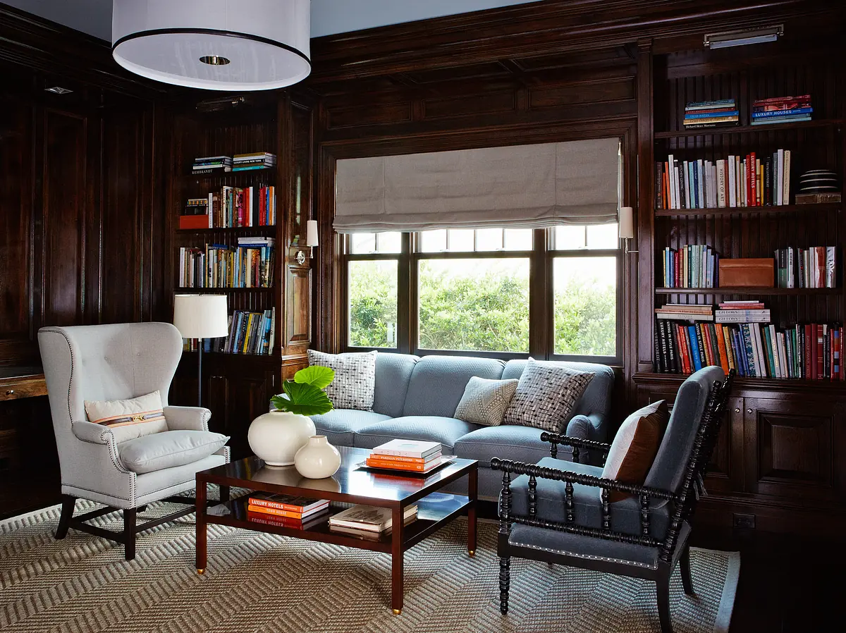 Living room with blue sofa, accent chairs, wood coffee table, area rug, bookshelves, and large window with roller shade.