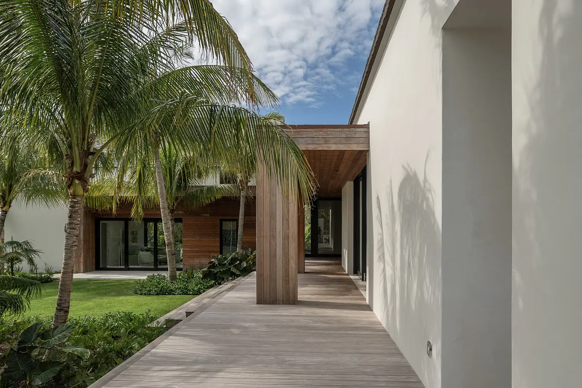 Front exterior with wooden walkway, palm trees, and large glass doors leading to the house.