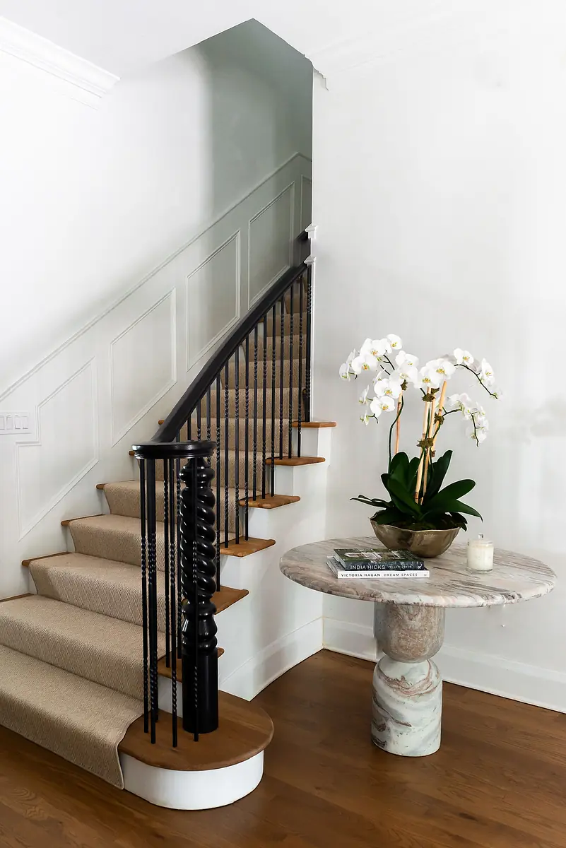 Foyer with staircase, round marble table, floral arrangement, and hardwood flooring.
