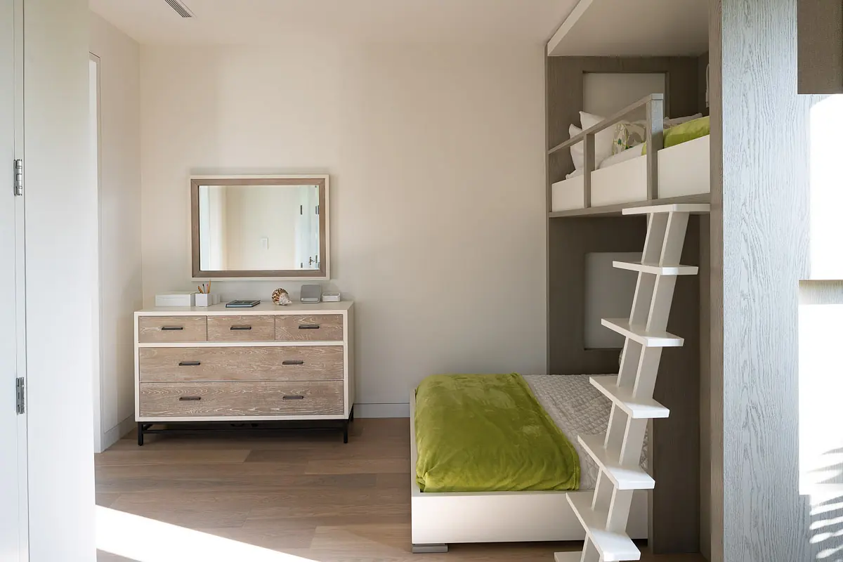 Bedroom with raised bed, green blanket, wooden dresser, wall mirror, and ladder for access.