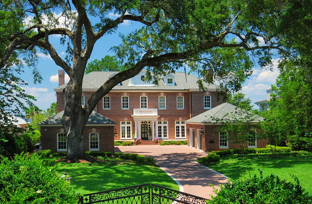 Front exterior of a two-story brick house with entryway, windows, porch, and large tree