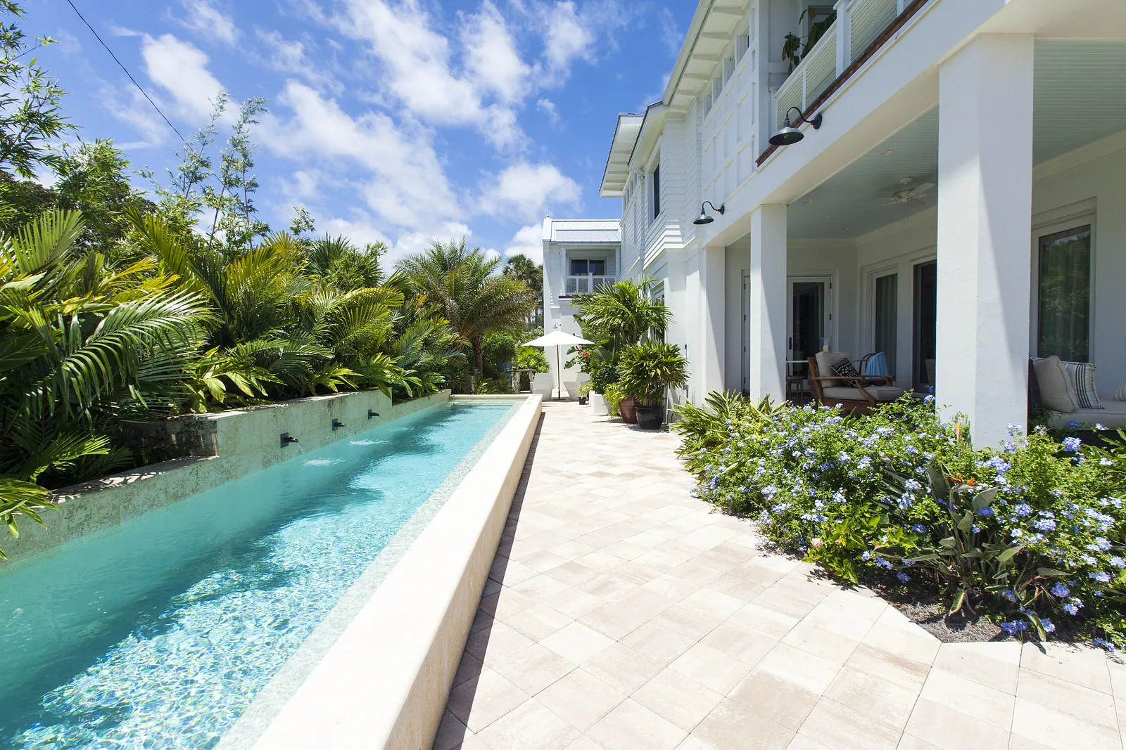 Exterior area with swimming pool, stone paving, tropical plants, and patio area with lounge chairs and umbrella