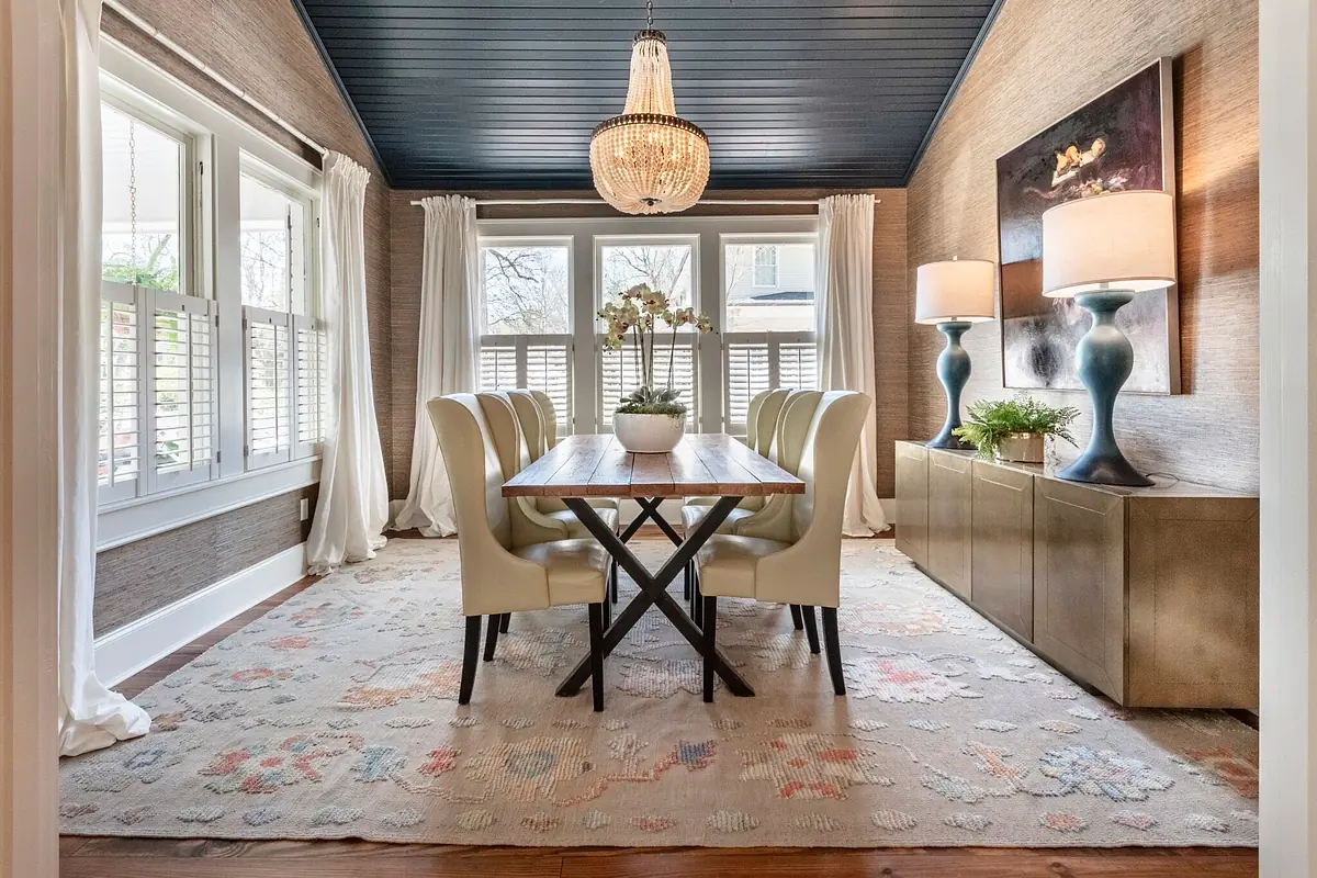 Dining room with wooden table, white chairs, console table, lamps, blue ceiling, and floral area rug