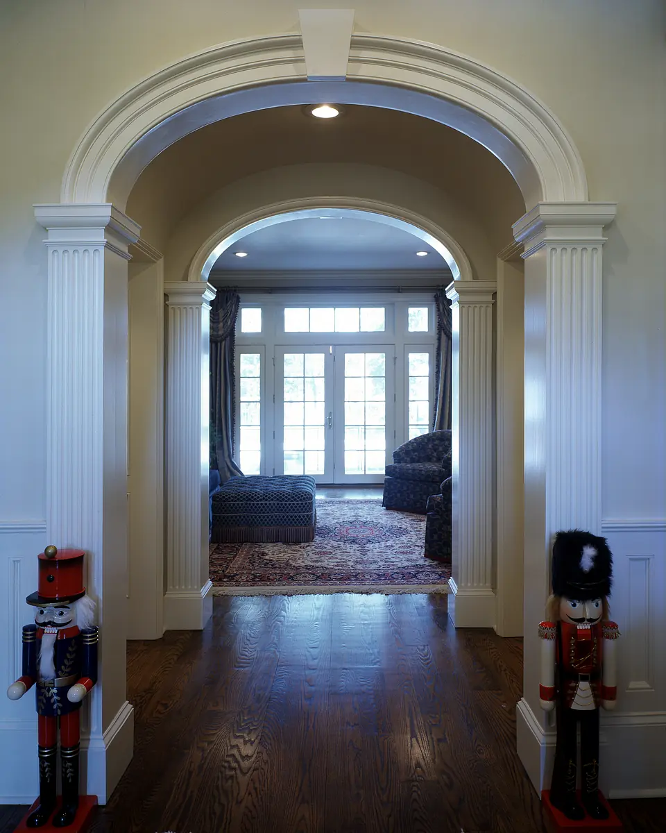 Hallway with arched entrance, nutcracker decorations, and view into a living room with large windows.
