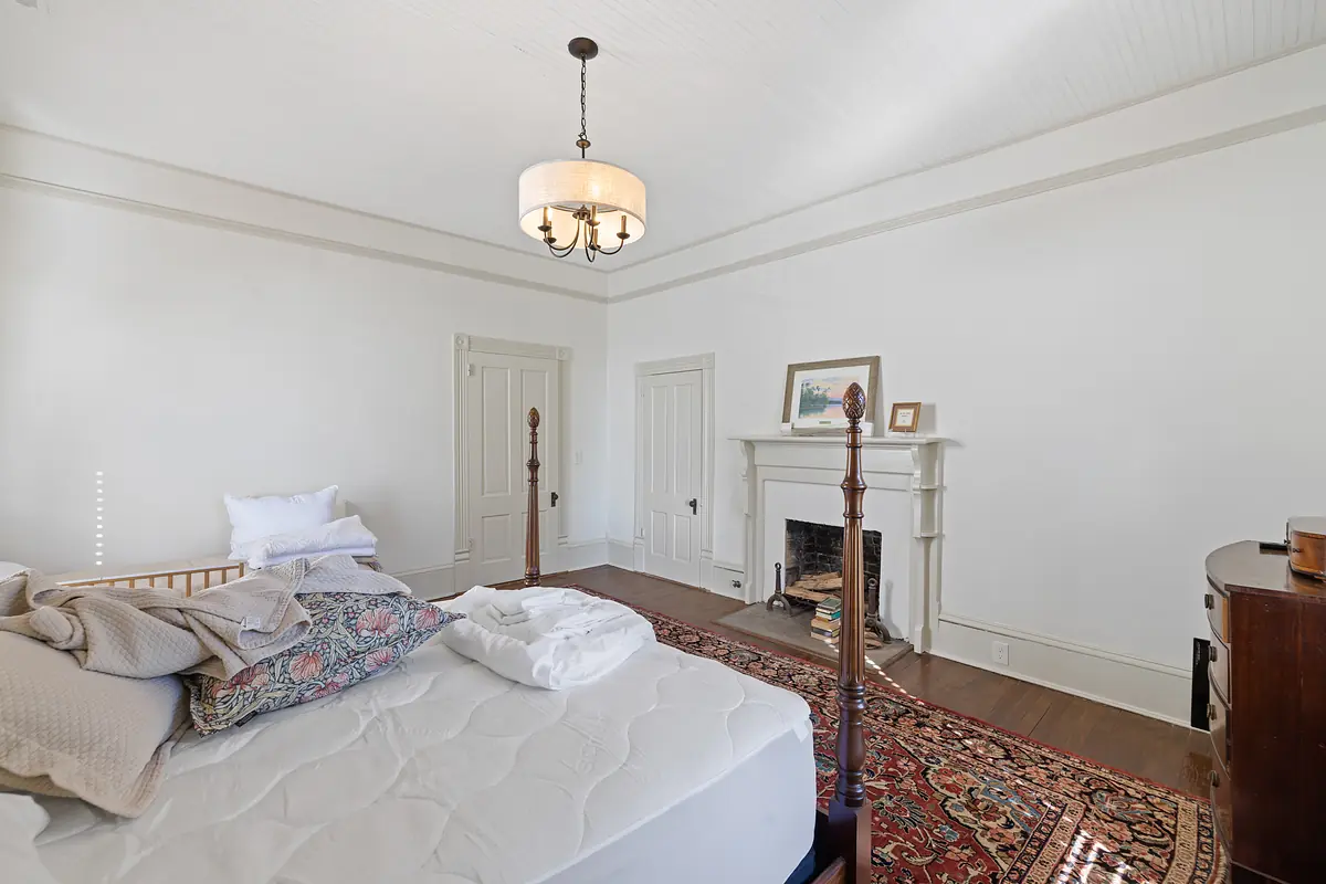 Bedroom with four-poster bed, fireplace, chest, and patterned area rug.
