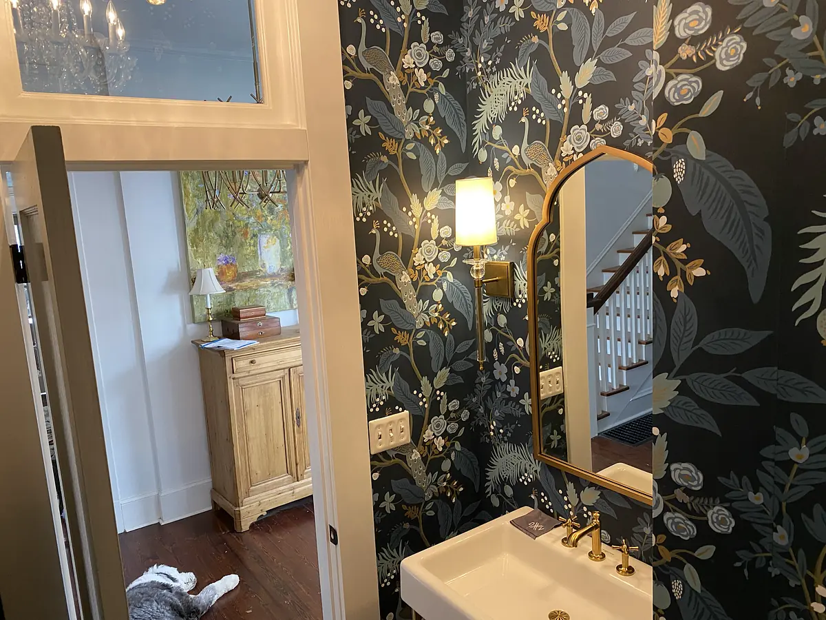 Powder room with floral wallpaper, mirror, sink, gold faucet, and wooden console table.