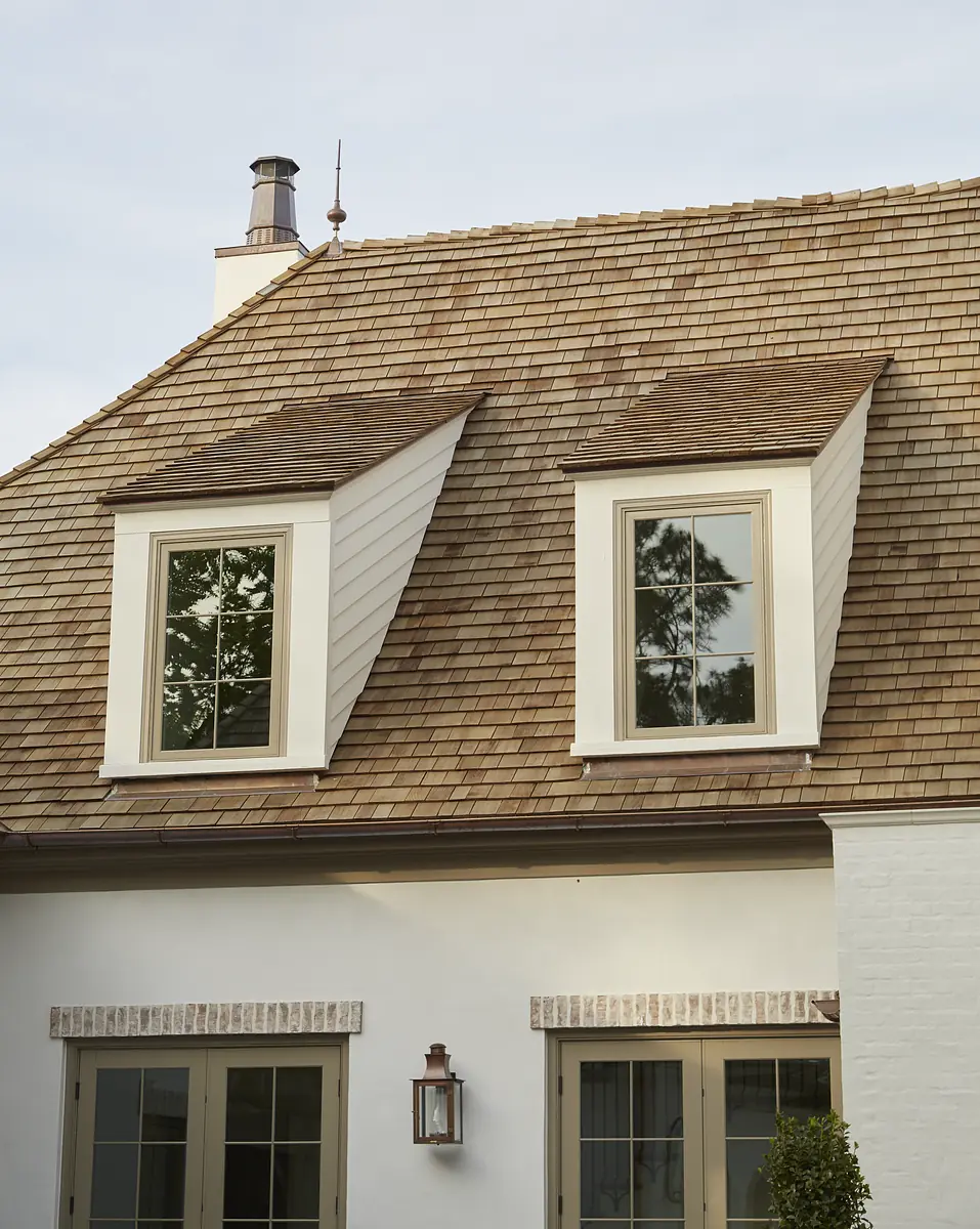 Exterior rear of house with sloped wooden shingle roof, two windows, and brick facade.