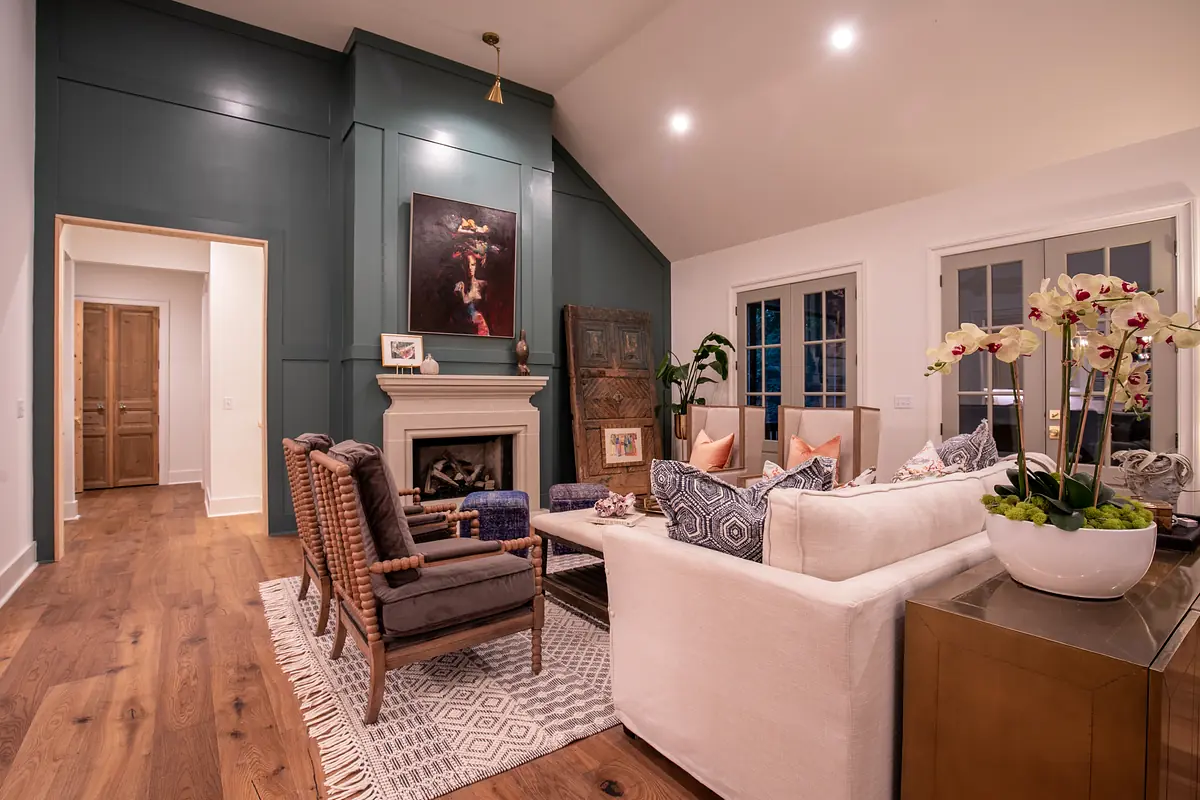 Living room with white sofa, chairs, coffee table, rug, fireplace, and large windows.