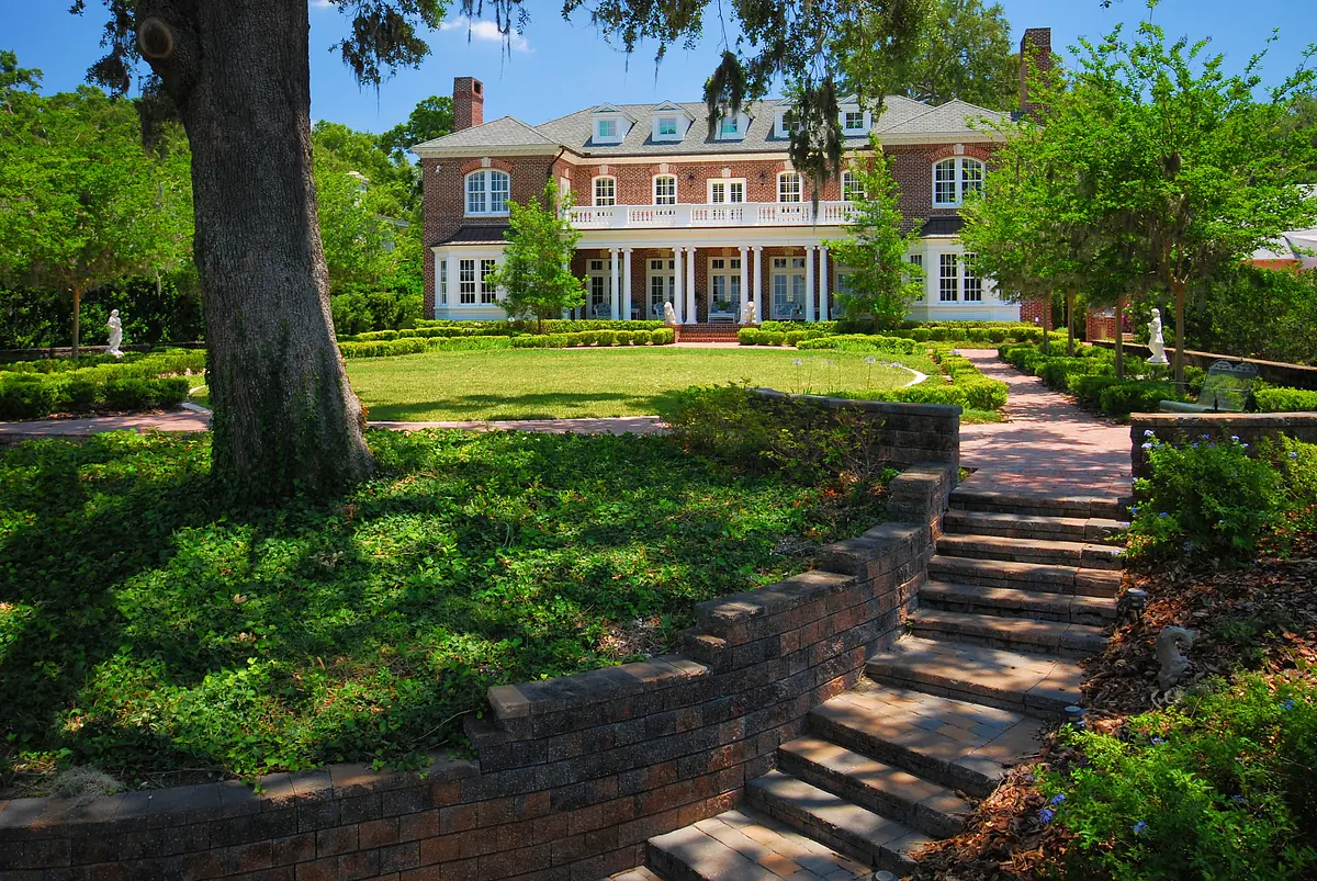 Front exterior view of a large brick house with landscaped garden and brick pathway.
