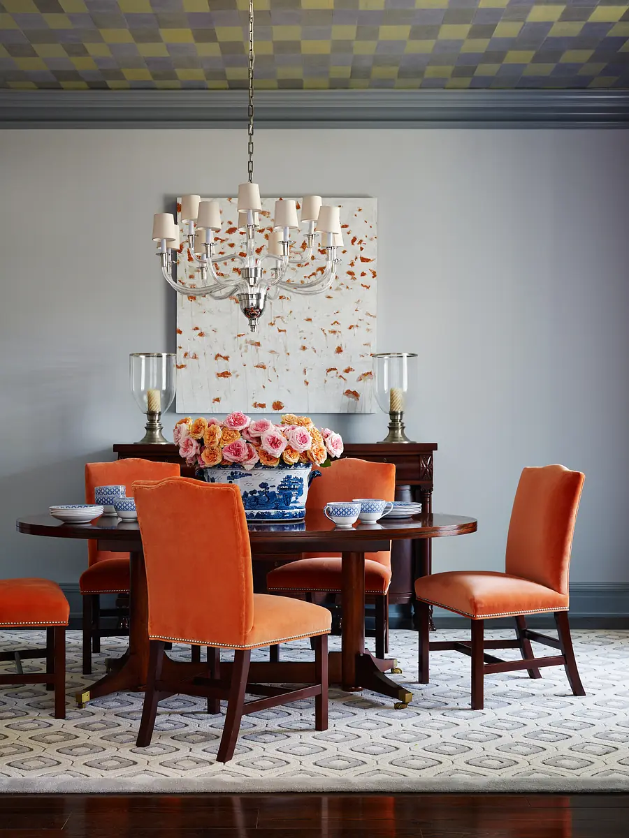 Dining room with round table, orange chairs, floral centerpiece, wall artwork, and chandelier