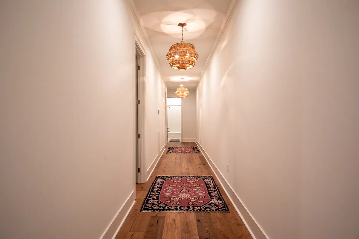 Hallway with hardwood flooring, area rugs, two woven light fixtures, and white walls.