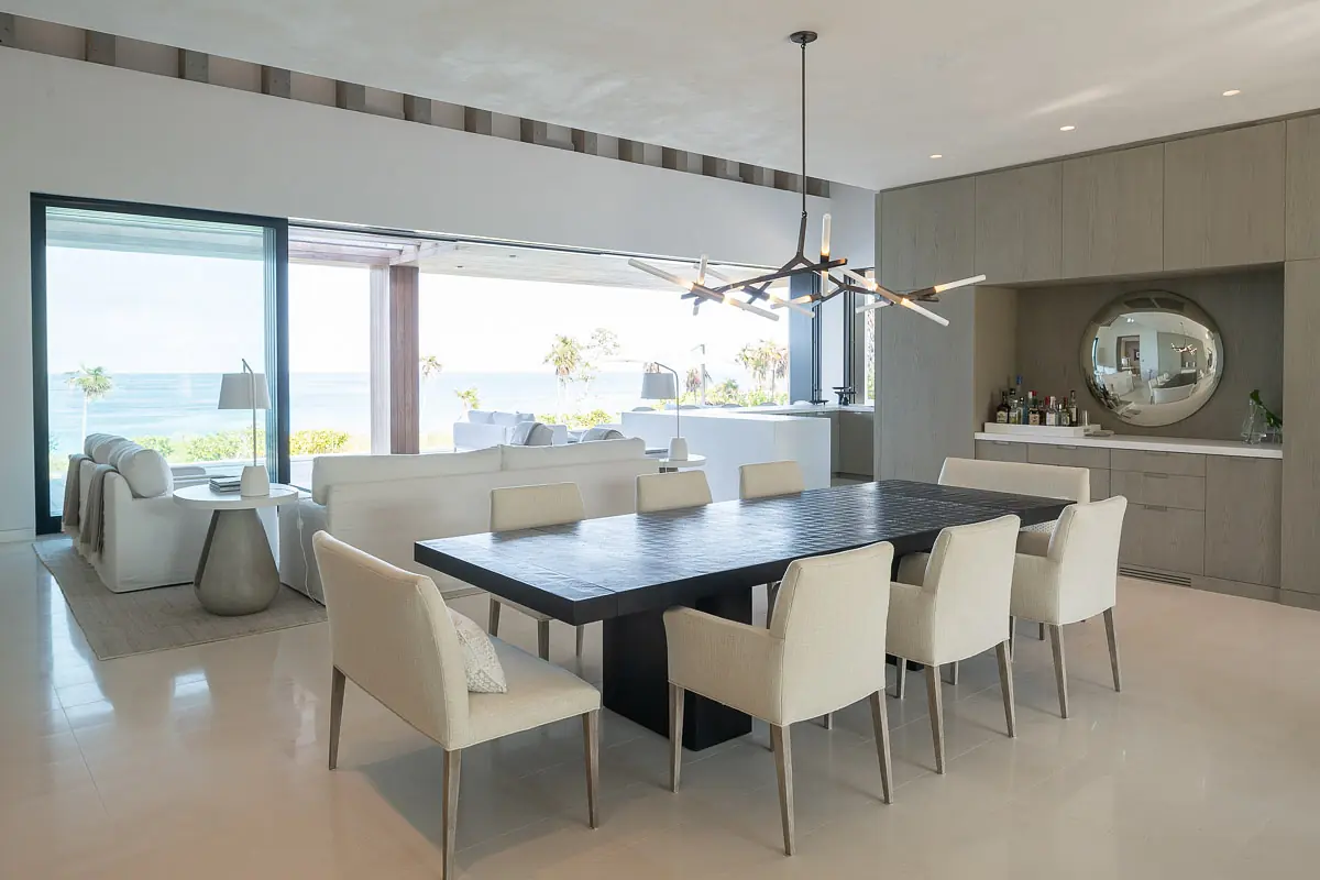 Dining room with black table, eight beige chairs, built-in buffet, round mirror, and large sliding doors to outdoors.