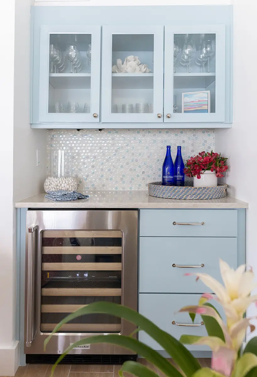 Butler's pantry with blue cabinets, marble countertop, wine cooler, and decorative glassware and flowers.